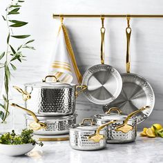 pots and pans are lined up on the counter next to a pot rack with gold handles