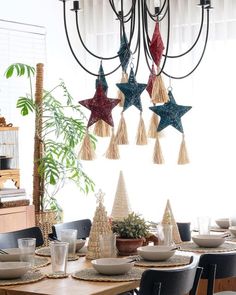 a dining room table set for christmas with decorations hanging from the chandelier above it