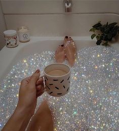 someone is sitting in the bathtub with their feet up and holding a coffee cup