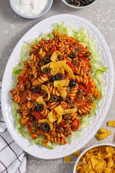 a white plate topped with pasta salad next to bowls of tortilla chips and dip