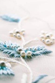 a close up view of some beads on a white fabric with blue leaves and snowflakes