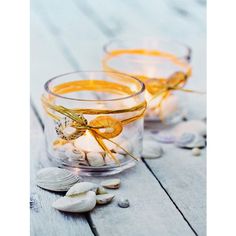 two glass cups filled with sea shells on top of a wooden table