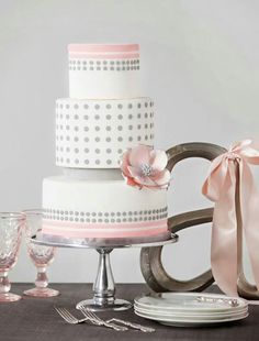 a white and pink wedding cake with polka dots on the top is surrounded by silverware