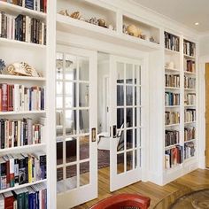 a living room filled with lots of books on top of white book shelves next to a red chair