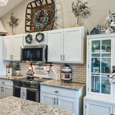 this kitchen has white cabinets and granite counter tops with christmas wreaths on the wall