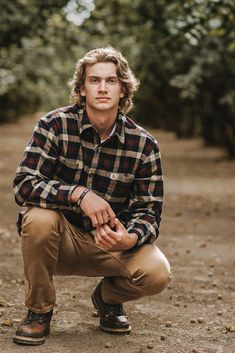 a man kneeling down in the dirt with his hands on his knees and looking at the camera