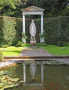 a statue in the middle of a pond surrounded by greenery and water lilies