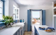 a kitchen with blue and white cabinets, counter tops, and sink in front of an open door