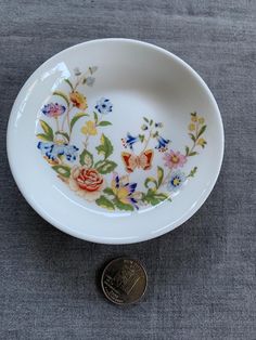 a white bowl with colorful flowers on it next to a penny