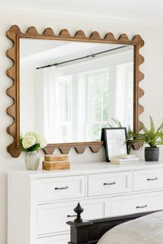 a white dresser topped with a mirror next to a window