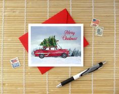 a red car with a christmas tree on top is sitting next to some stamps and a pen