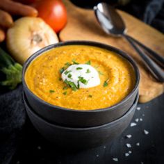 there is a bowl of soup on the table next to some vegetables and utensils