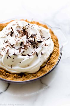 a pie with whipped cream and chocolate shavings on top sits on a marble surface