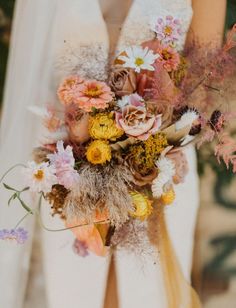 a woman holding a bouquet of flowers in her hands and wearing a white wedding dress