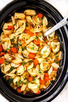 a crock pot filled with tortellini shells, carrots and parsley