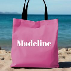 a pink shopping bag with the word madeline printed on it sitting in the sand