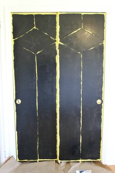 a black door with yellow paint on it in front of a white wall and brown floor