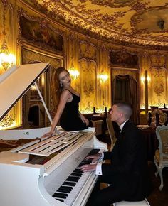 a woman in a black dress sitting at a piano with a man standing next to her