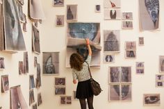 a woman standing in front of a wall covered with pictures and holding her hand up