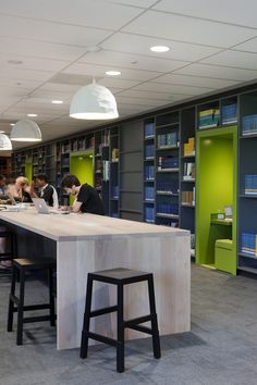 people sitting at tables in a library with bookshelves and shelves full of books