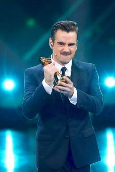 a man in a suit and tie holding an award for best performance at the oscars