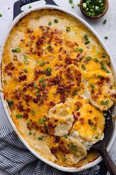 a casserole dish filled with potatoes, bacon and green onions next to a bowl of peas