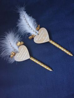 two heart shaped toothbrushes with white feathers and gold trimmings on them