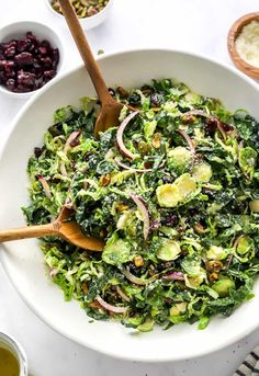 a white bowl filled with green salad and wooden spoons