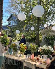 a group of people standing around a table with vases and flowers in front of them