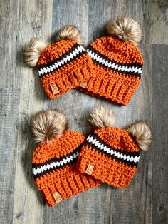 two knitted hats with pom - poms are laying on a wood floor