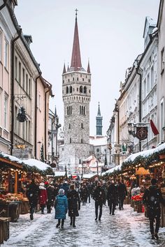 people are walking through an old town during the winter season with snow on the ground and buildings in the background