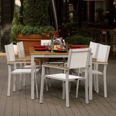 an outdoor dining table and chairs set up on a brick patio with potted plants in the background