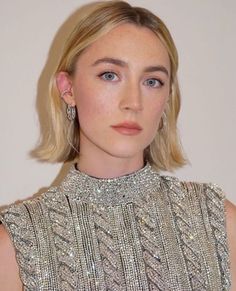 a woman with blonde hair and blue eyes wearing a silver dress is looking at the camera