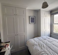 a white bed sitting next to a window in a bedroom under a light fixture on a wall