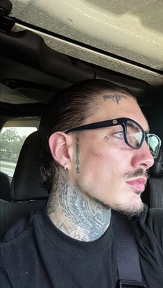 a man with tattoos and glasses sitting in the back seat of a car looking at something