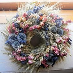 a wreath made out of dried flowers and grass is hanging on the door frame in front of a window