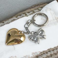 two heart shaped keychains sitting on top of a white and gold pillow next to each other