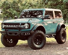 a large green truck parked on top of a gravel road next to trees and grass