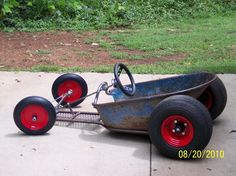 an old metal cart with red wheels on the sidewalk in front of some grass and bushes