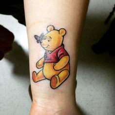 a small winnie the pooh tattoo on the wrist is shown in yellow and red