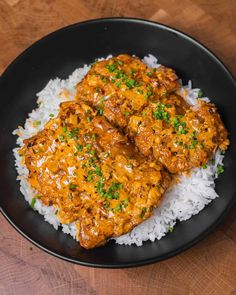 two pieces of chicken on top of rice in a black plate with green garnish