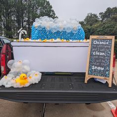 the back of a pickup truck filled with water bottles and rubber ducky toys next to a chalkboard sign