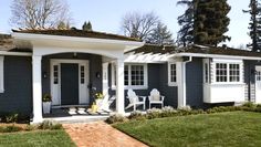 a gray house with white trim on the front door and porch, along with two lawn chairs