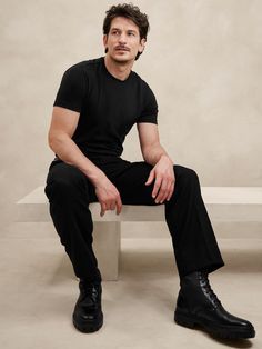 a man sitting on top of a white bench next to a cement wall and wearing black shoes