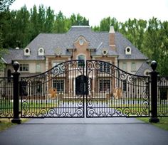 an iron gate in front of a large house with a driveway leading to the entrance