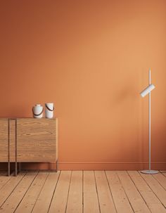 an orange wall with two white vases on it and a wooden dresser in the foreground