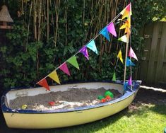 a boat filled with sand and colorful flags sitting in the grass next to a fence