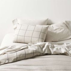 an unmade bed with two pillows on top of it and a white wall in the background