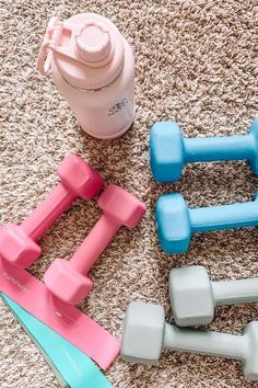 three dumbs, one blue and one pink are laying on the floor next to a water bottle