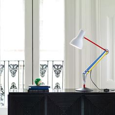 a desk lamp sitting on top of a black dresser next to a window with white curtains